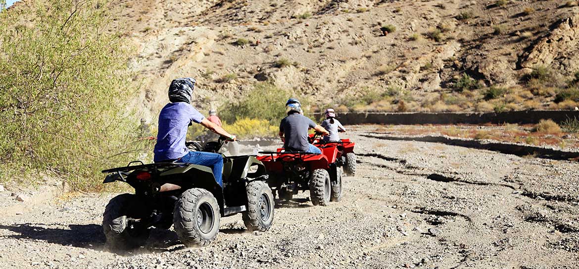 Three people driving ATVs through a desert landscape