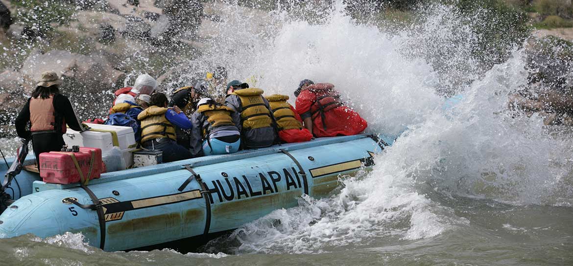 Waves crashing onto passengers aboard a blue raft