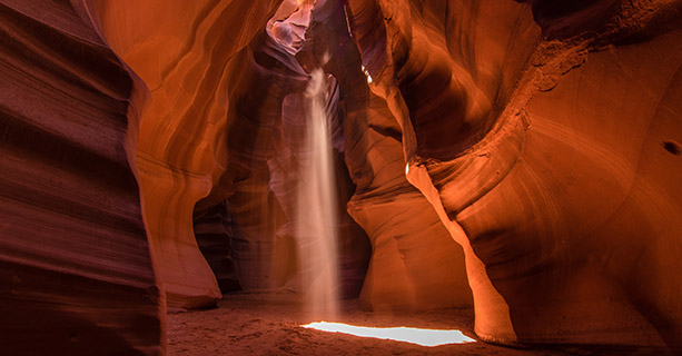 Sunlight beams into an orange canyon cave.