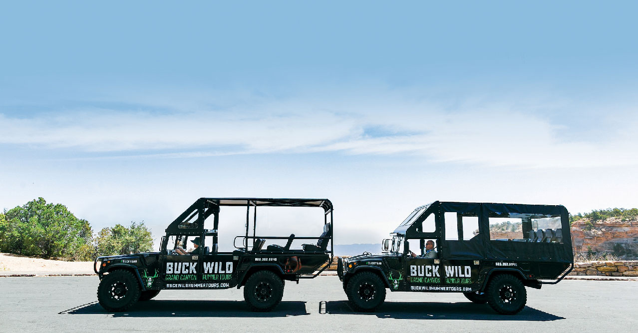 Two Hummer vehicles parked in front of a Grand Canyon viewpoint.