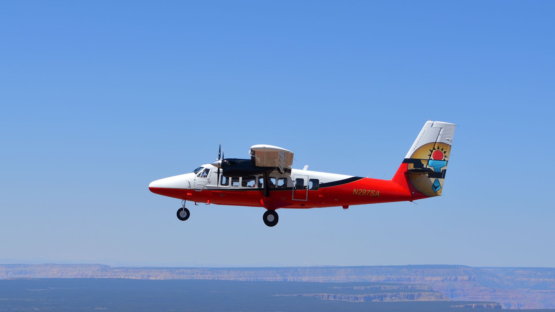 A Twin Otter airplane soars through a clear blue sky.