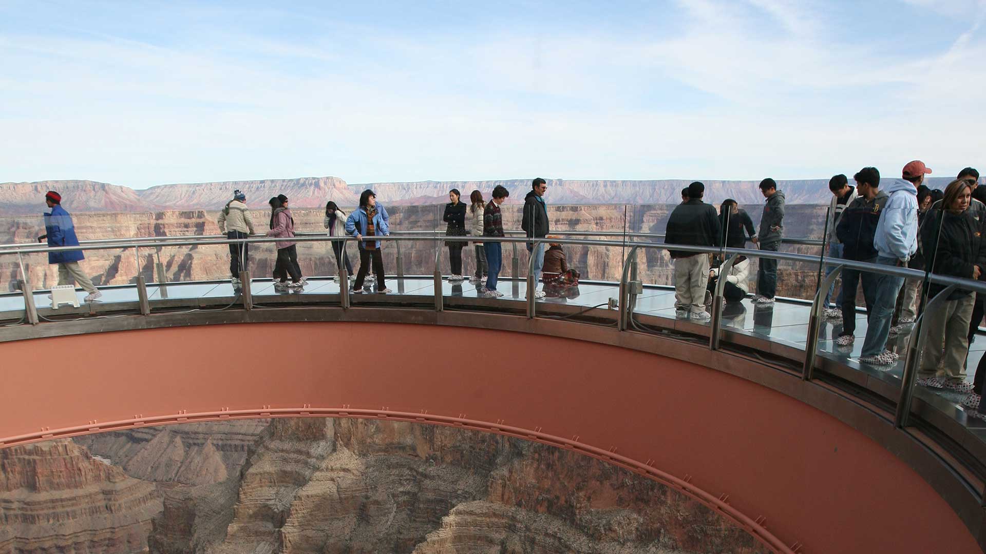 Visitors to the Grand Canyon West stand atop the Skywalk Bridge with canyon scenery behind them.