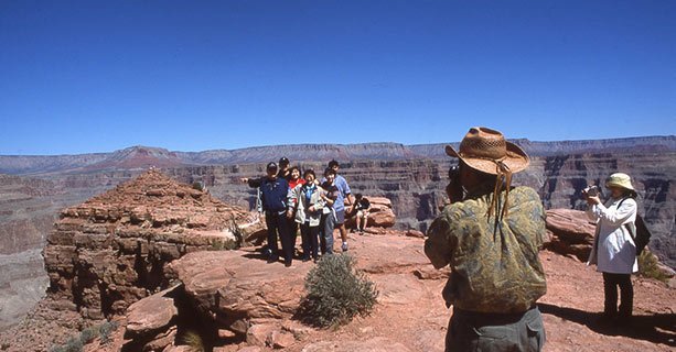 A group poses for a photo in front of a Grand Canyon viewpoint.