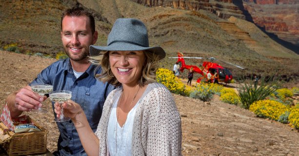 Two passengers enjoy a champagne toast on the Grand Canyon floor with a helicopter in the background.