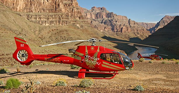 A helicopter landed at the bottom of the Grand Canyon with the Colorado River behind it.