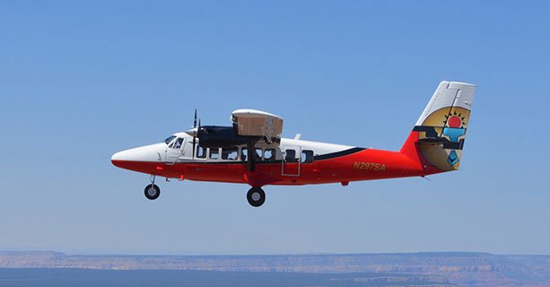 An airplane soars through a clear sky over the Grand Canyon.