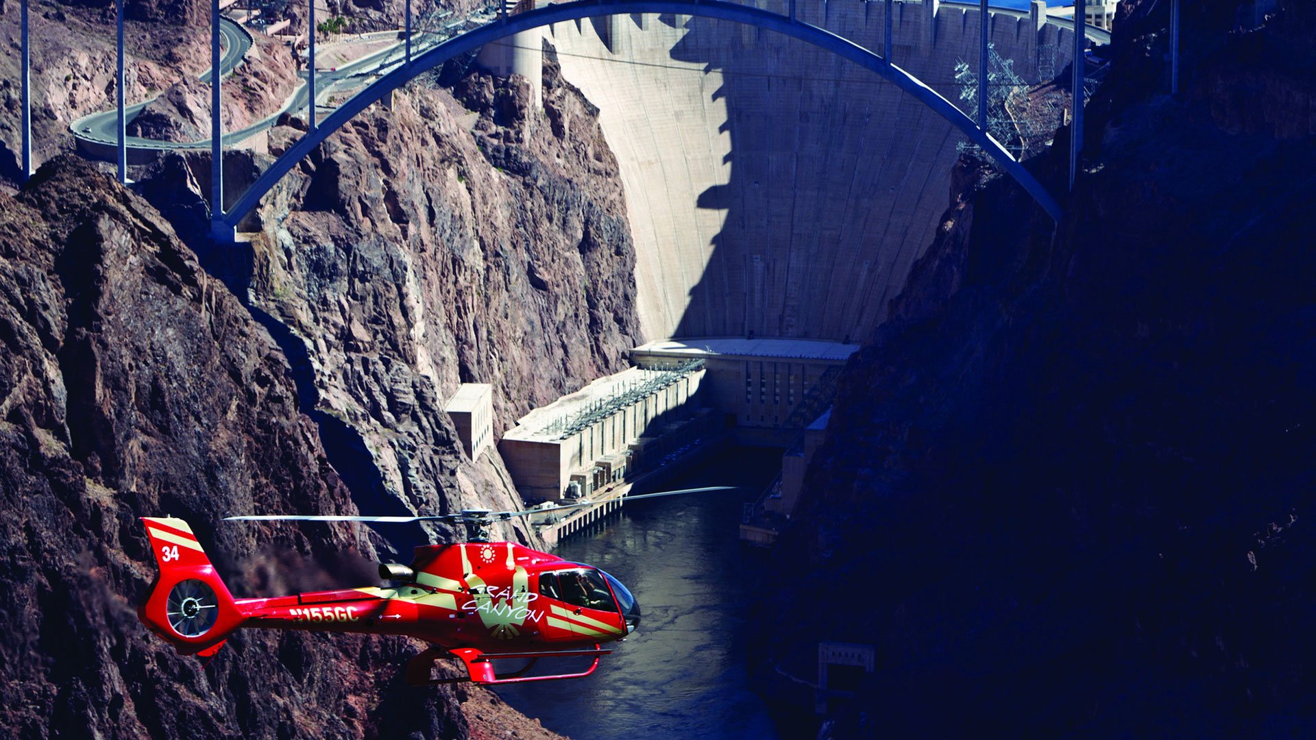 A red helicopter soars in front of Hoover Dam.