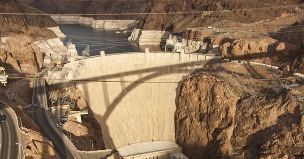 Hoover Dam lit by the sun with the shadow of a bridge cast across its face.