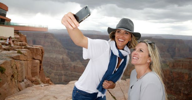 Two women pose for a photo with the Grand Canyon and Skywalk Bridge behind them.