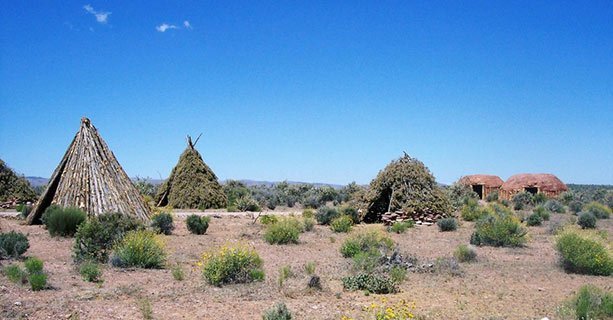 Several traditional Native American dwellings surrounded by a desert landscape.