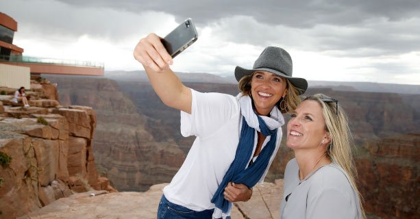 Two women pose for a photo at the canyon's edge with the Skywalk behind them.