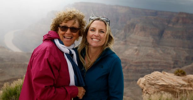 Two women pose smiling at the edge of the Grand Canyon West.