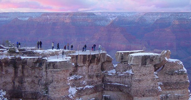 Visitors standing atop a snow-capped ledge at the Grand Canyon.