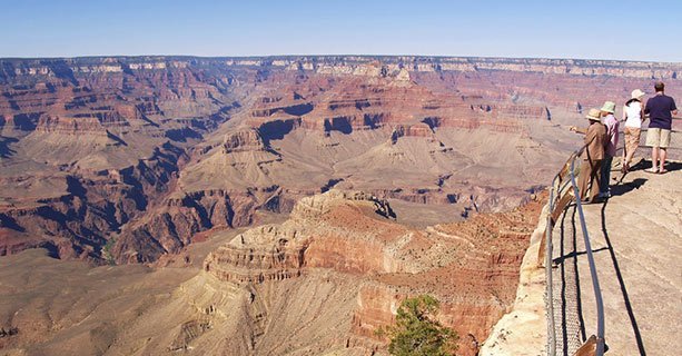 A group of sightseers stand at the edge of a Grand Canyon viewpoint.