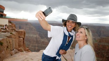 Two women take a photo together at the canyon's edge with the Skywalk Bridge behind them.