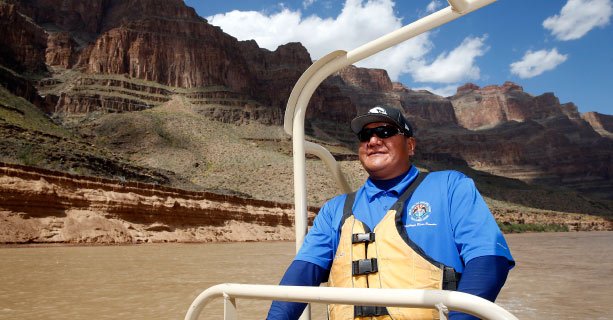 A driver steering a pontoon boat down the Colorado River through the Grand Canyon.