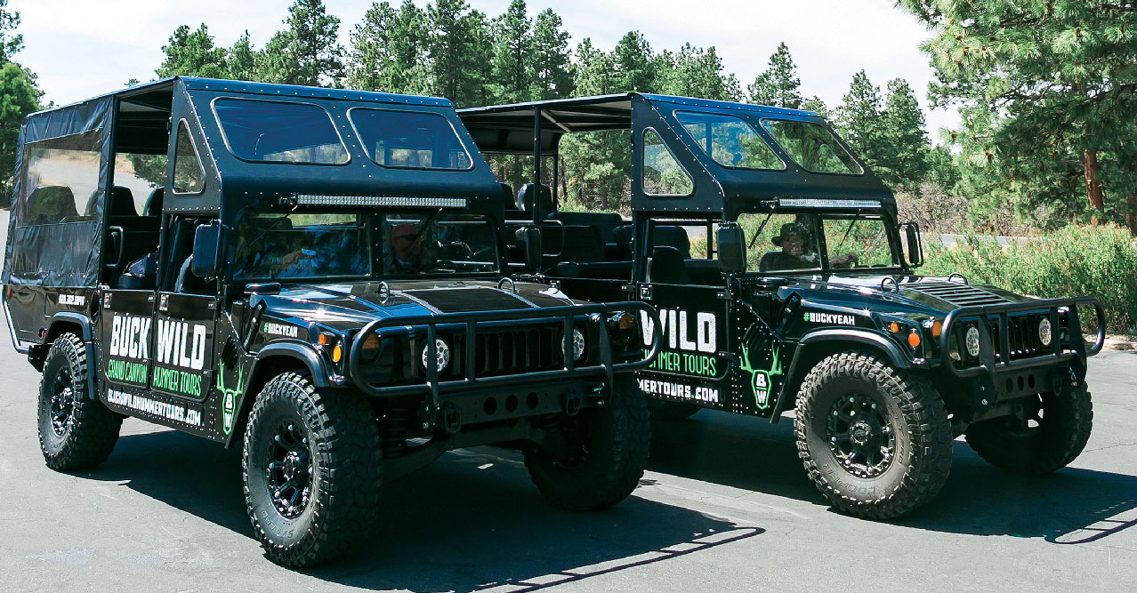 Two Hummer touring vehicles parked against a forested backdrop.