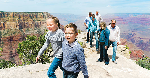 A family wanders a Grand Canyon viewpoint with children in the foreground.