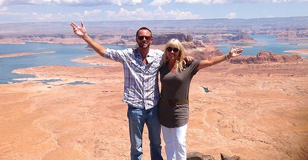 Two helicopter tour passengers standing atop Tower Butte with Lake Powell in the background.