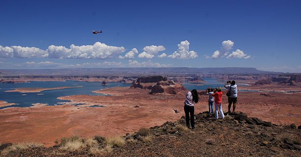 Passengers stand at the edge of Tower Butte as a helicopter soars by.