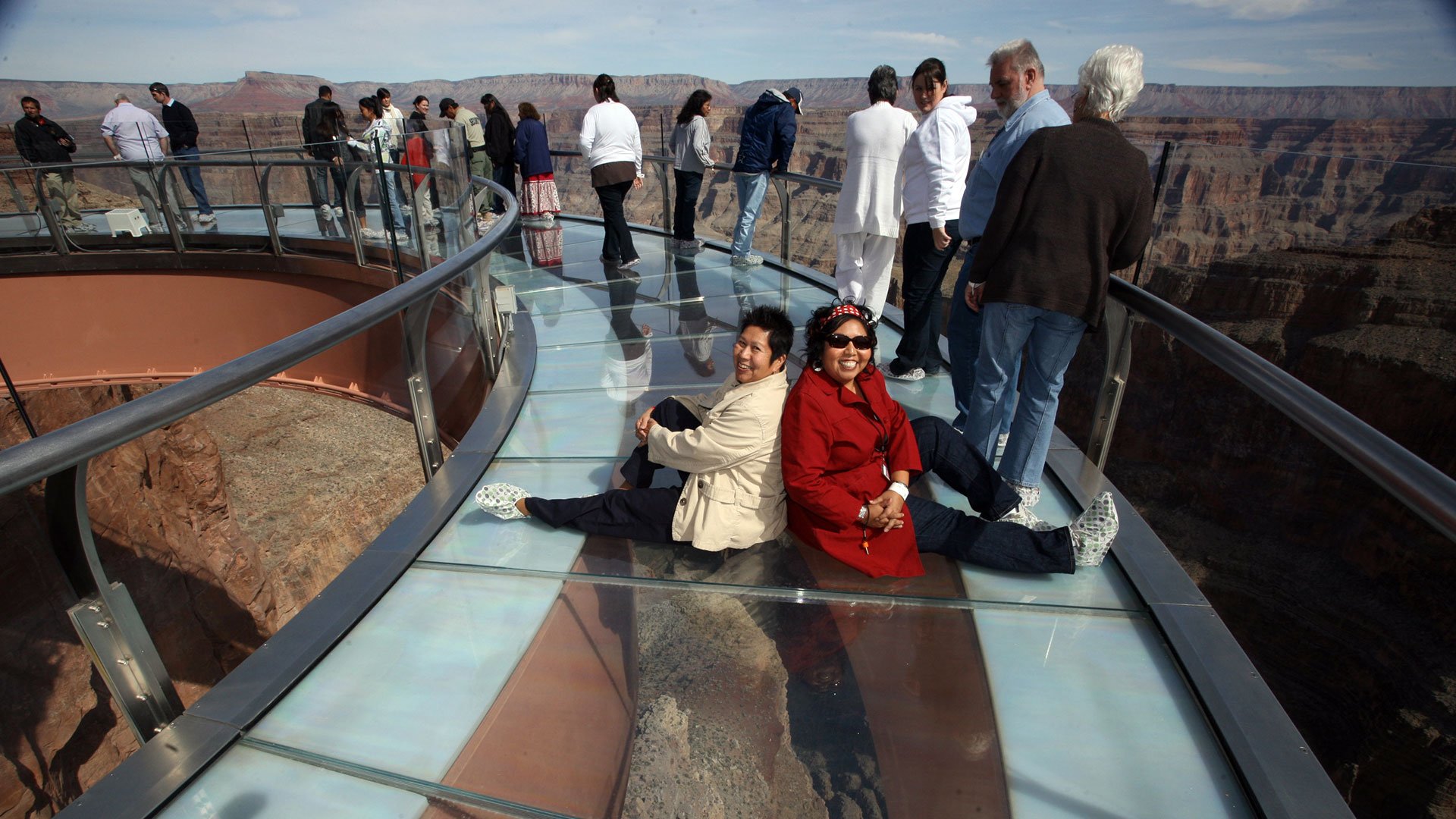 Two women sitting on the glass floor of the Skywalk posing for a photo.