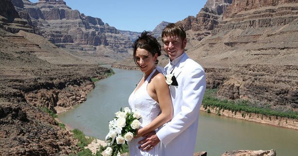 Bride and groom stand in front of the Colorado River on canyon floor.