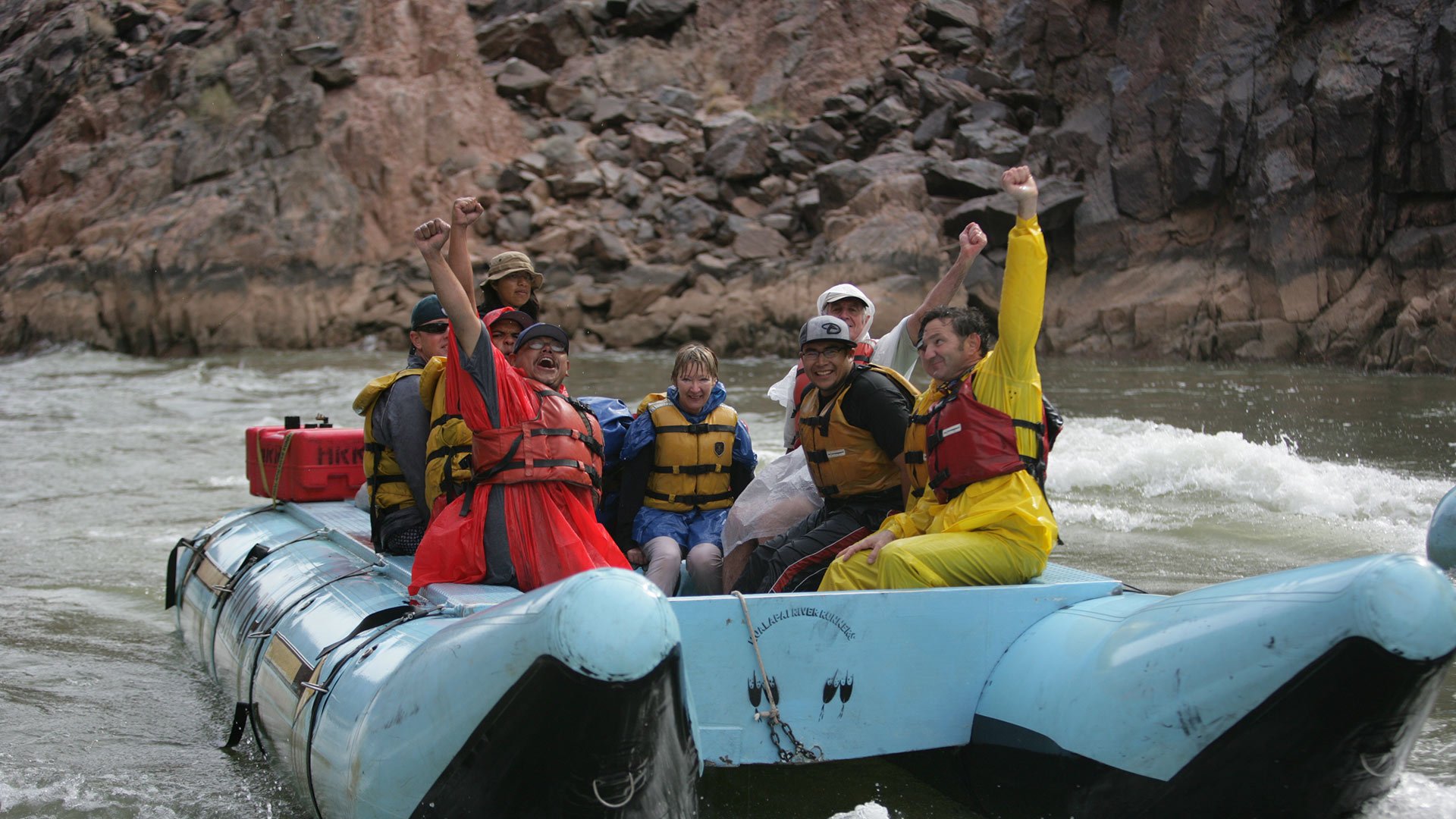 A group of passengers cheer aboard a raft on the Colorado River.