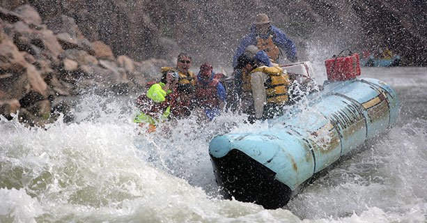 Passengers laugh aboard a rafting tour splashing through the Colorado River.